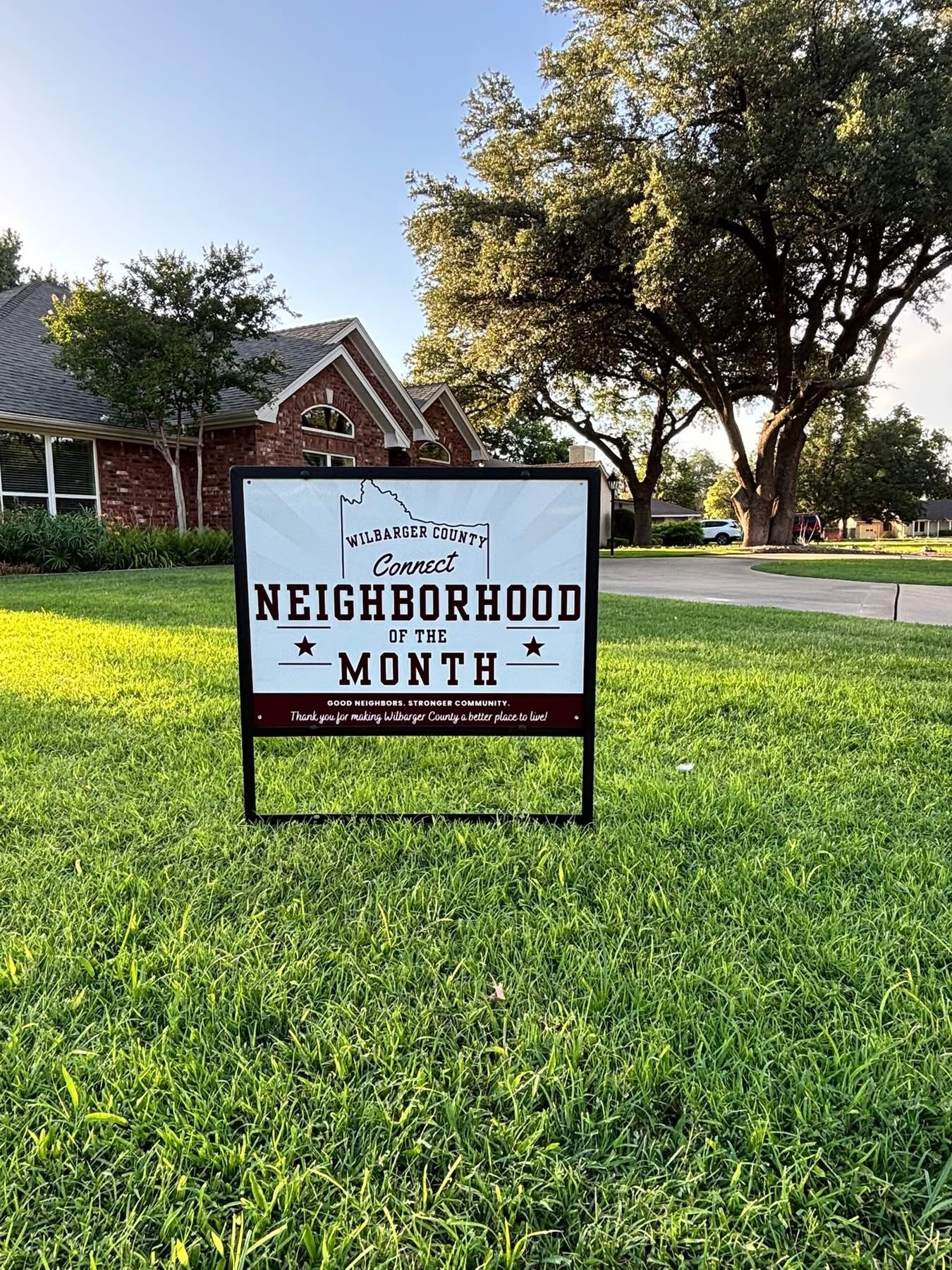 Wilbarger County Neighborhood of the Month yard sign in front of a brick home on Bell Street with a large shade tree
